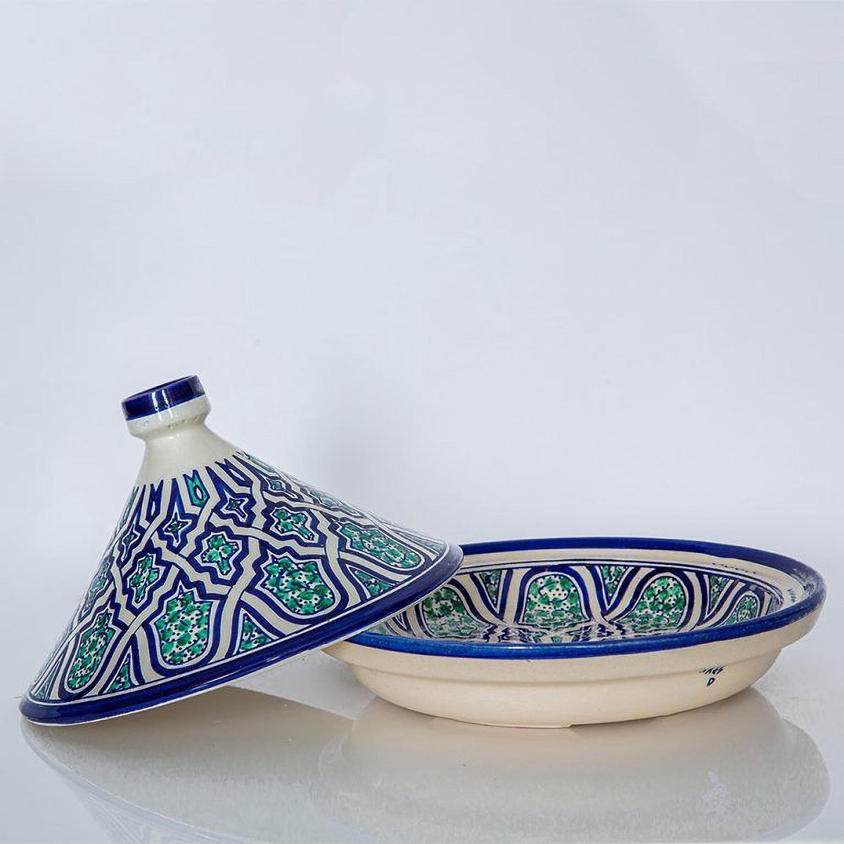 A white ceramic bowl with a blue and green patterned lid and a matching bowl with a similar patterned lid are placed on a white surface.