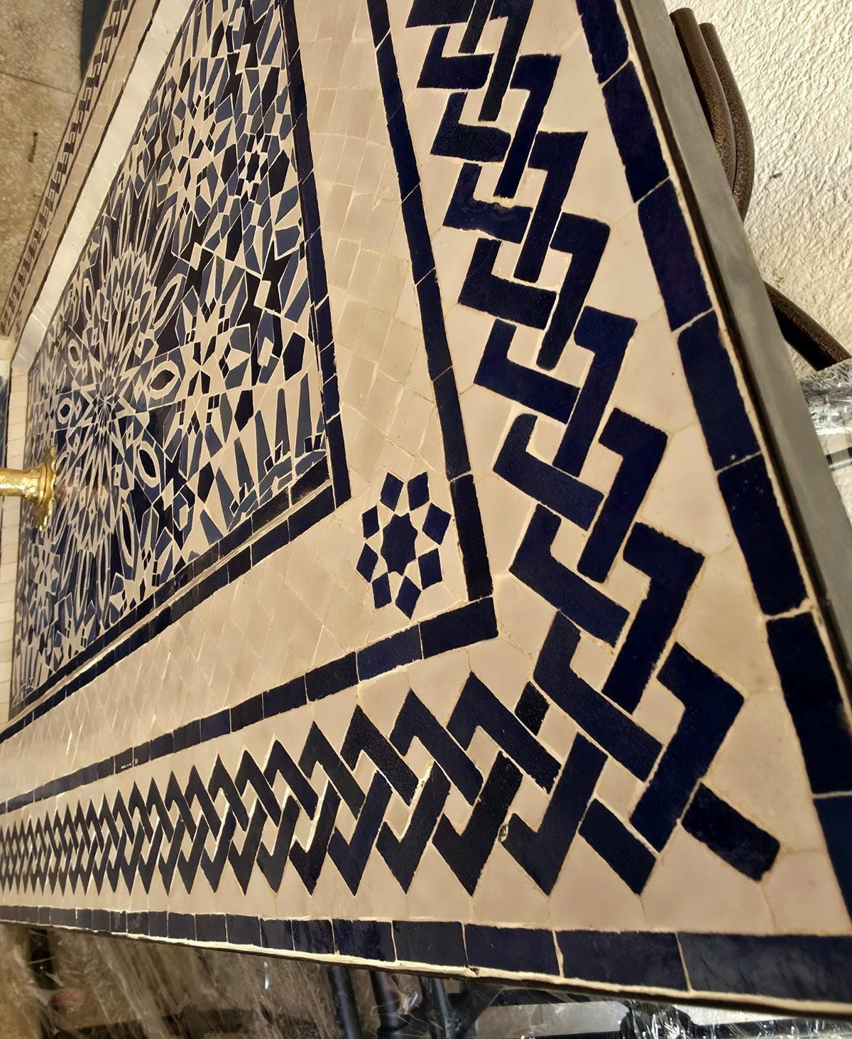 Detail of the interlaced navy and white braided border framing the mosaic fountain, showing the precise hand set zellige tilework.