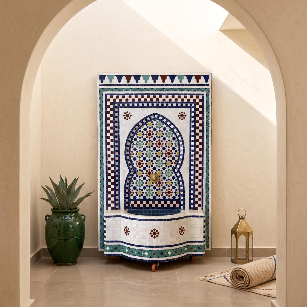 a decorative fountain with a mosaic design, surrounded by a green vase, a lantern, and a rug, all set against a beige wall with an arched doorway.