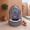 a decorative fountain with a blue and gold mosaic design, situated in a courtyard with a pool and potted plants.