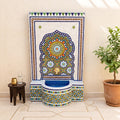 a colorful mosaic fountain with a blue and white base, surrounded by a potted plant and a small table.