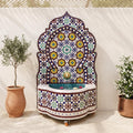 a decorative fountain with a mosaic design, surrounded by potted plants and a terracotta pot.