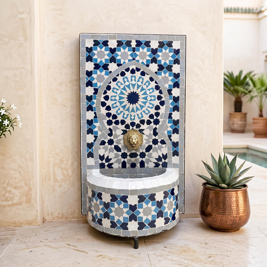 a decorative fountain with a mosaic design, placed on a tiled floor next to a potted plant.