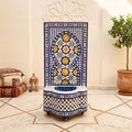 a decorative tile fountain with a blue and white mosaic design, situated in a room with a tiled floor and a potted plant.