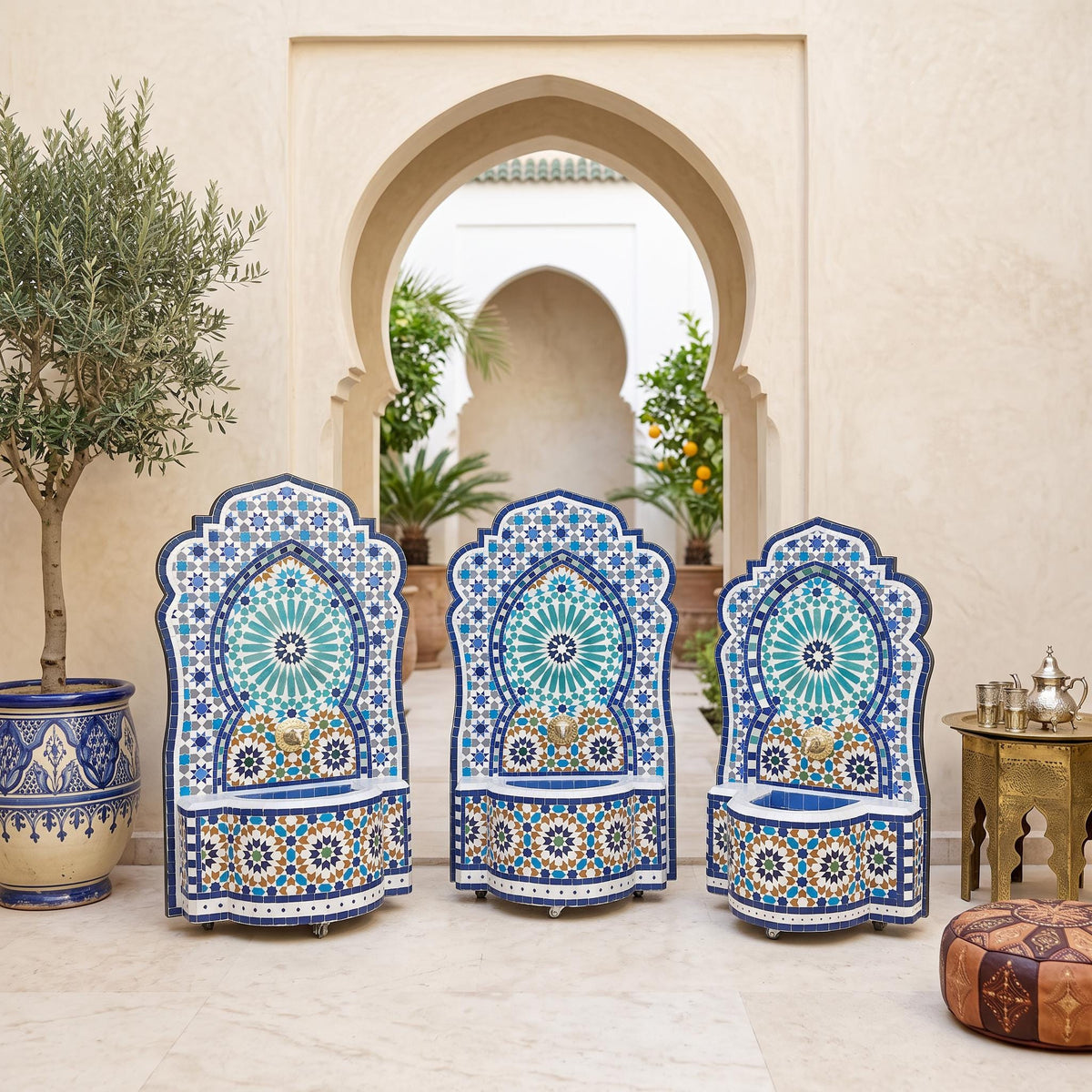 a courtyard with three ornate chairs adorned with blue and white mosaic patterns, situated in front of a doorway with arches. The chairs are surrounded by potted plants, and a small table is visible on the right side of the image.