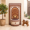 a decorative fountain with a tree-like design, surrounded by potted plants and a wooden stool.