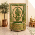 a decorative fountain with a green and gold mosaic design, situated in a room with a potted plant and other decorative elements.
