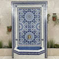 Handmade Moroccan mosaic wall fountain in blue and white zellige tile, front view, with a large geometric star pattern panel, brass lion head spout, and octagonal tiled basin against a stone wall.