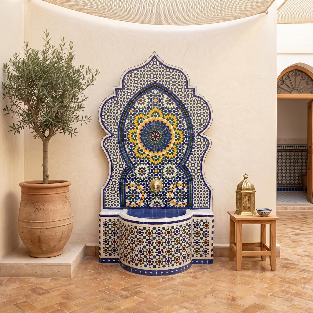 a decorative fountain with a mosaic design, surrounded by a potted plant and a small table with a bowl on it.