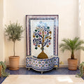 a decorative fountain with a tree design, surrounded by potted plants and a blue and white tiled wall.