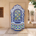 a decorative tile fountain with a blue and white mosaic design, situated in a room with arched doorways and a window.