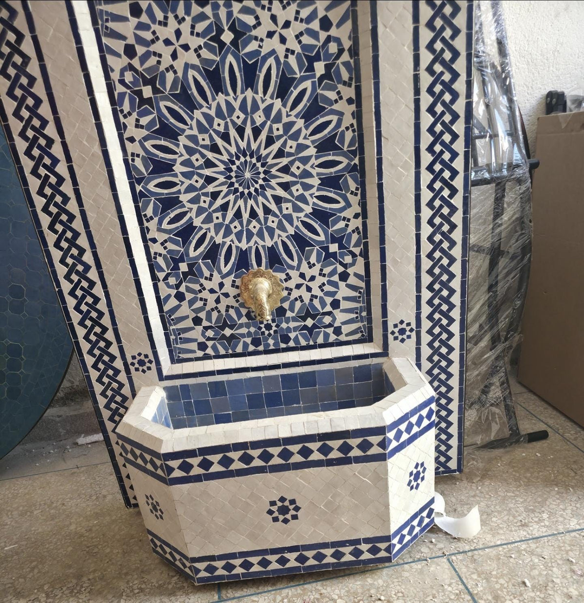 Detail of the antique brass lion head spout mounted at the center of the blue and white zellige panel, with water flowing into the basin below.
