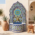 a decorative fountain with a mosaic design, surrounded by potted plants and a wooden table.