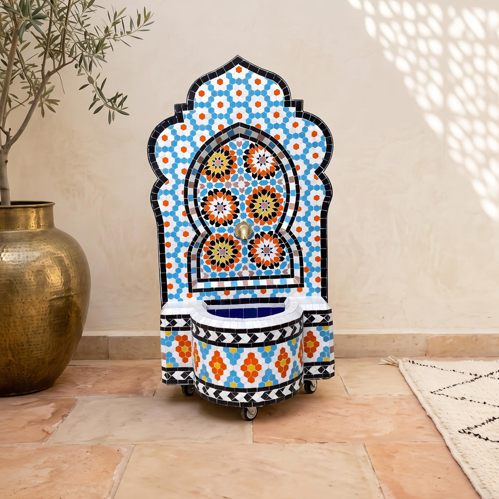 a colorful mosaic fountain with a blue and orange floral pattern, placed on a tiled floor next to a large gold vase.