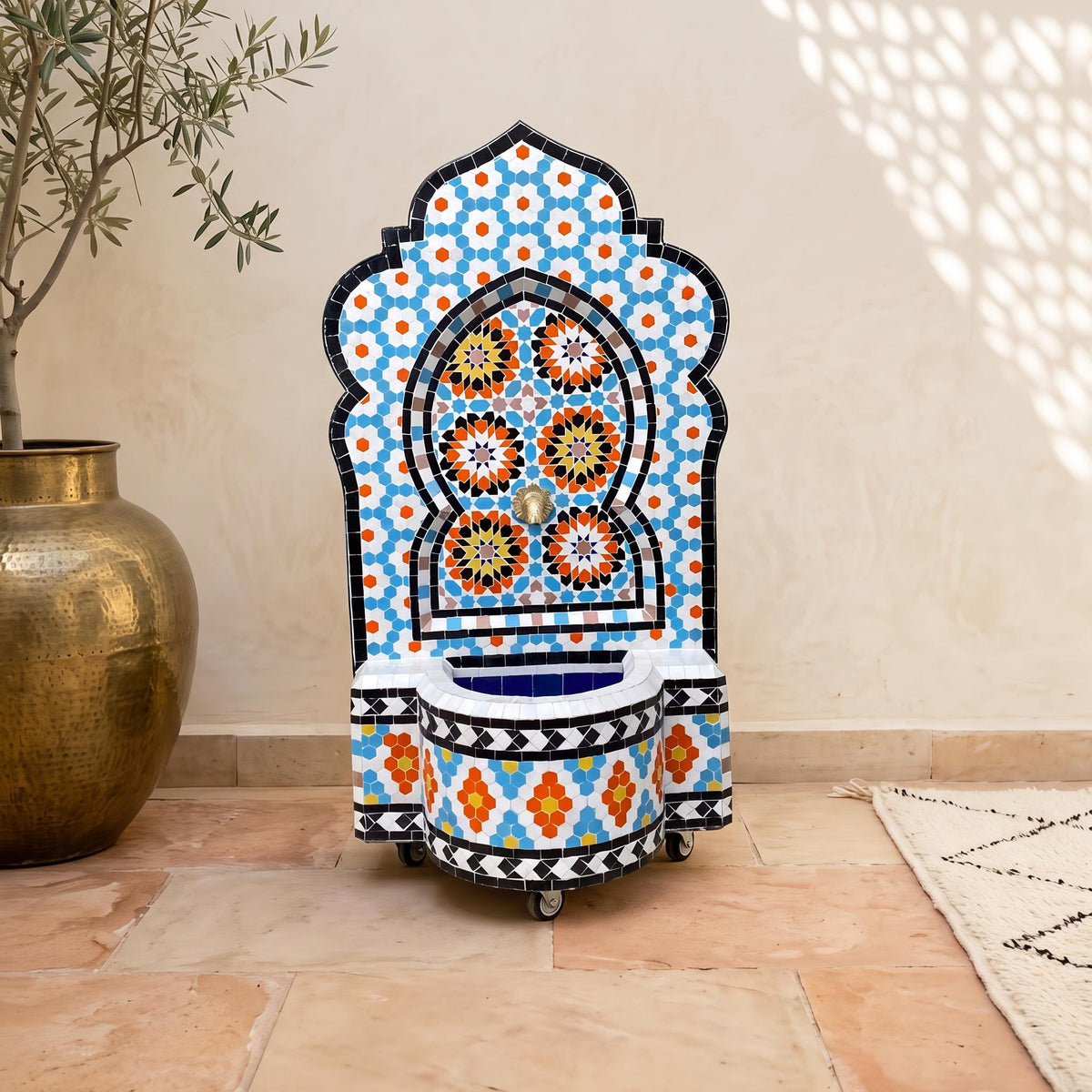 a colorful mosaic fountain with a blue and orange floral pattern, placed on a tiled floor next to a large gold vase.