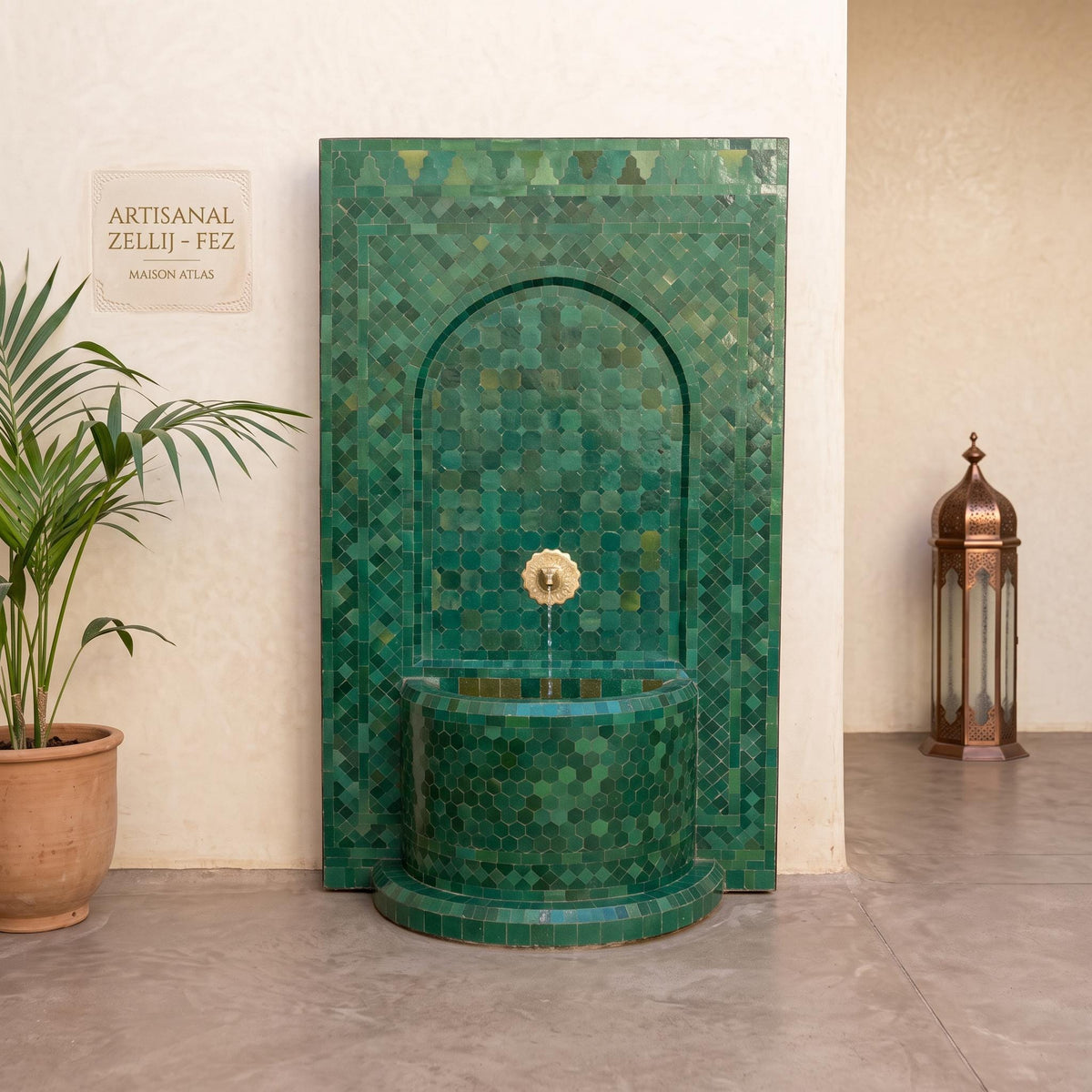 a green mosaic tile fountain with a white stone plaque above it, situated in a room with a potted plant and a lantern.