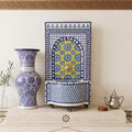 a decorative tile wall with a blue and white vase, a metal teapot, and a decorative tile fountain.