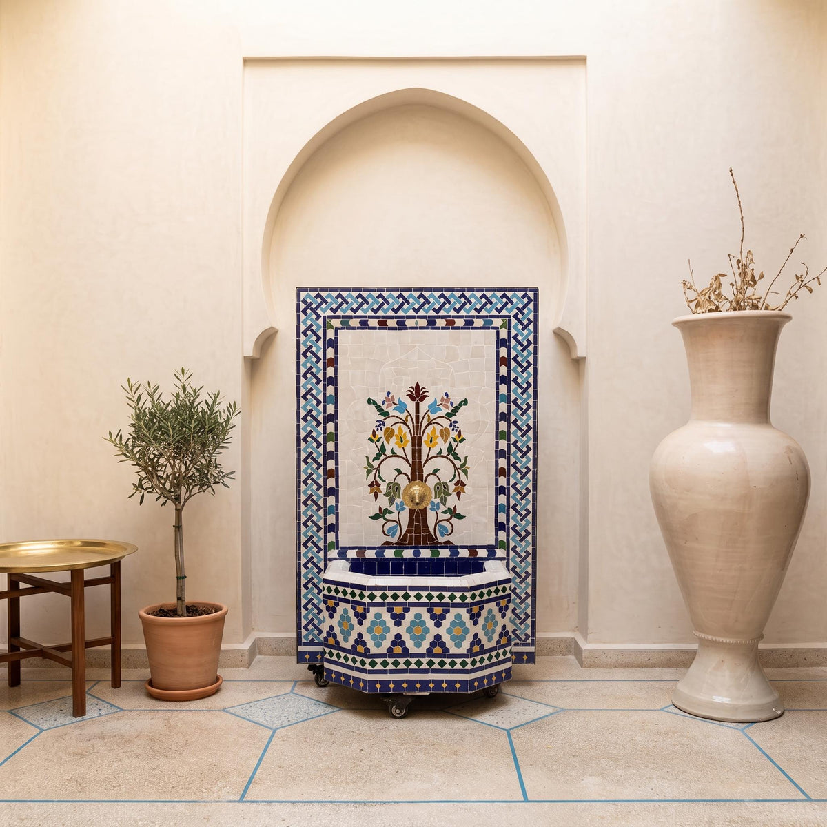 a decorative tile fountain with a blue and white border, situated in a room with a white archway. The room also includes a table with a plant and a large white vase.