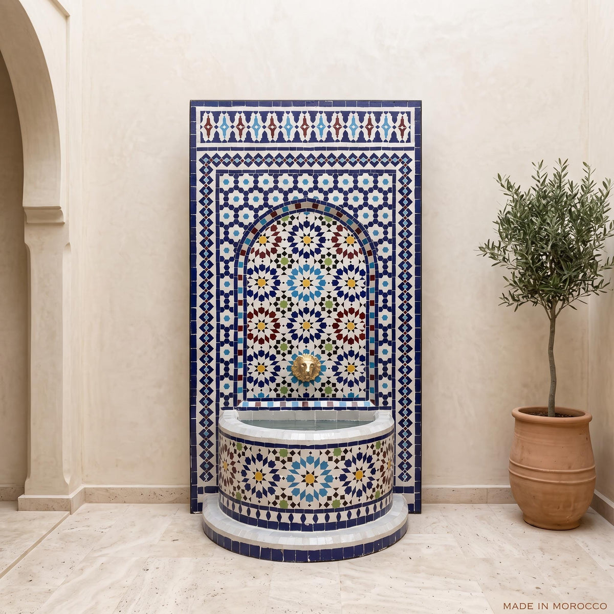 a decorative tile fountain with a blue and white mosaic design, situated in a room with a potted plant and a wall.