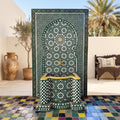 a decorative fountain with a mosaic tile design, situated in a courtyard with a bench and palm trees in the background.