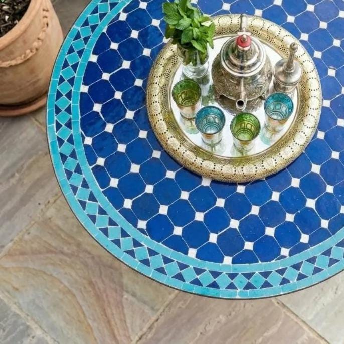 a blue and white patterned table with a metal tray holding a teapot, cups, and a plant.