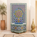 a decorative mosaic fountain with a blue and white tile design, situated in a room with a potted plant and a brass lamp.