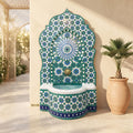 a decorative fountain with a mosaic design in shades of blue and green, situated in a courtyard. Next to the fountain is a potted plant, and the background includes a lattice structure and a wall.