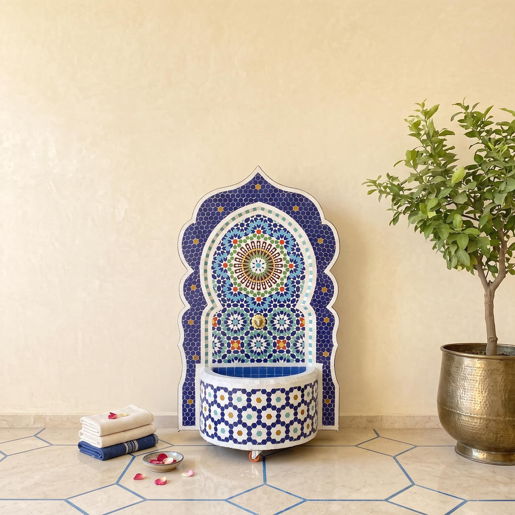 a decorative mosaic fountain with a blue and white pattern, placed on a tiled floor next to a potted plant.