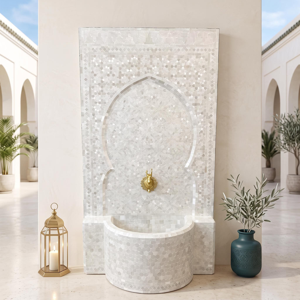 a white mosaic fountain with a gold faucet, situated in a courtyard with arched doorways and potted plants.