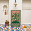 a room with a green and gold decorative tile wall, a wooden table with a teapot and cups, and a colorful tiled floor.