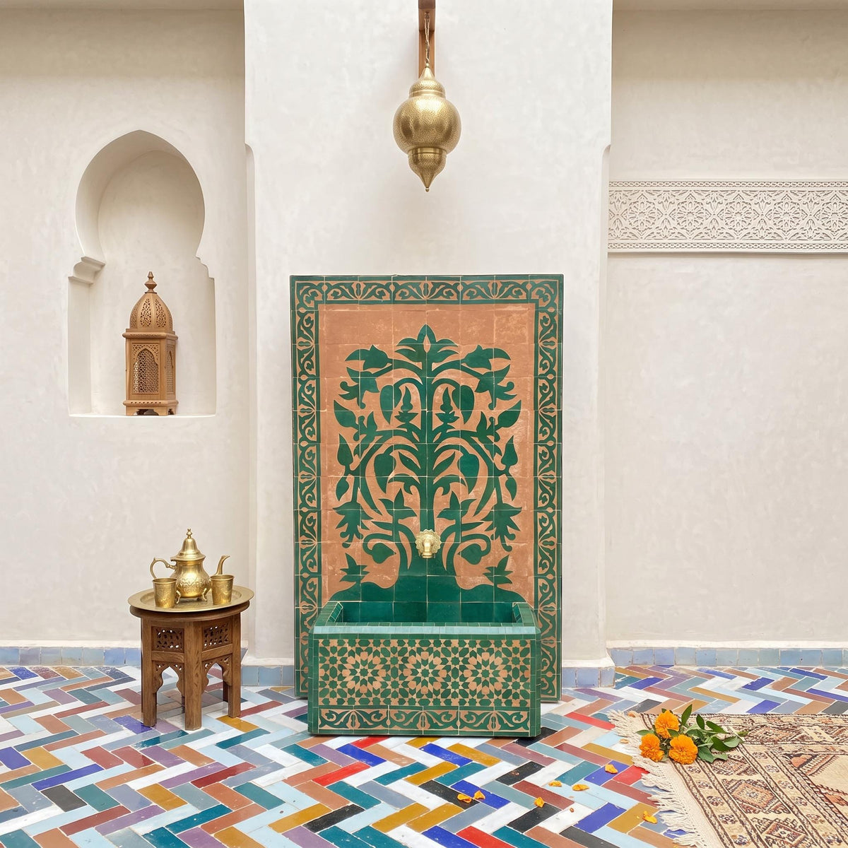 a room with a green and gold decorative tile wall, a wooden table with a teapot and cups, and a colorful tiled floor.