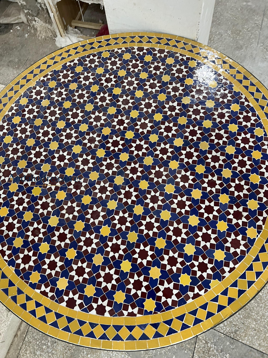 a circular tile floor with a vibrant geometric pattern in shades of blue, yellow, and red. The pattern consists of numerous small square tiles arranged in a repeating design, creating a visually striking and intricate design.