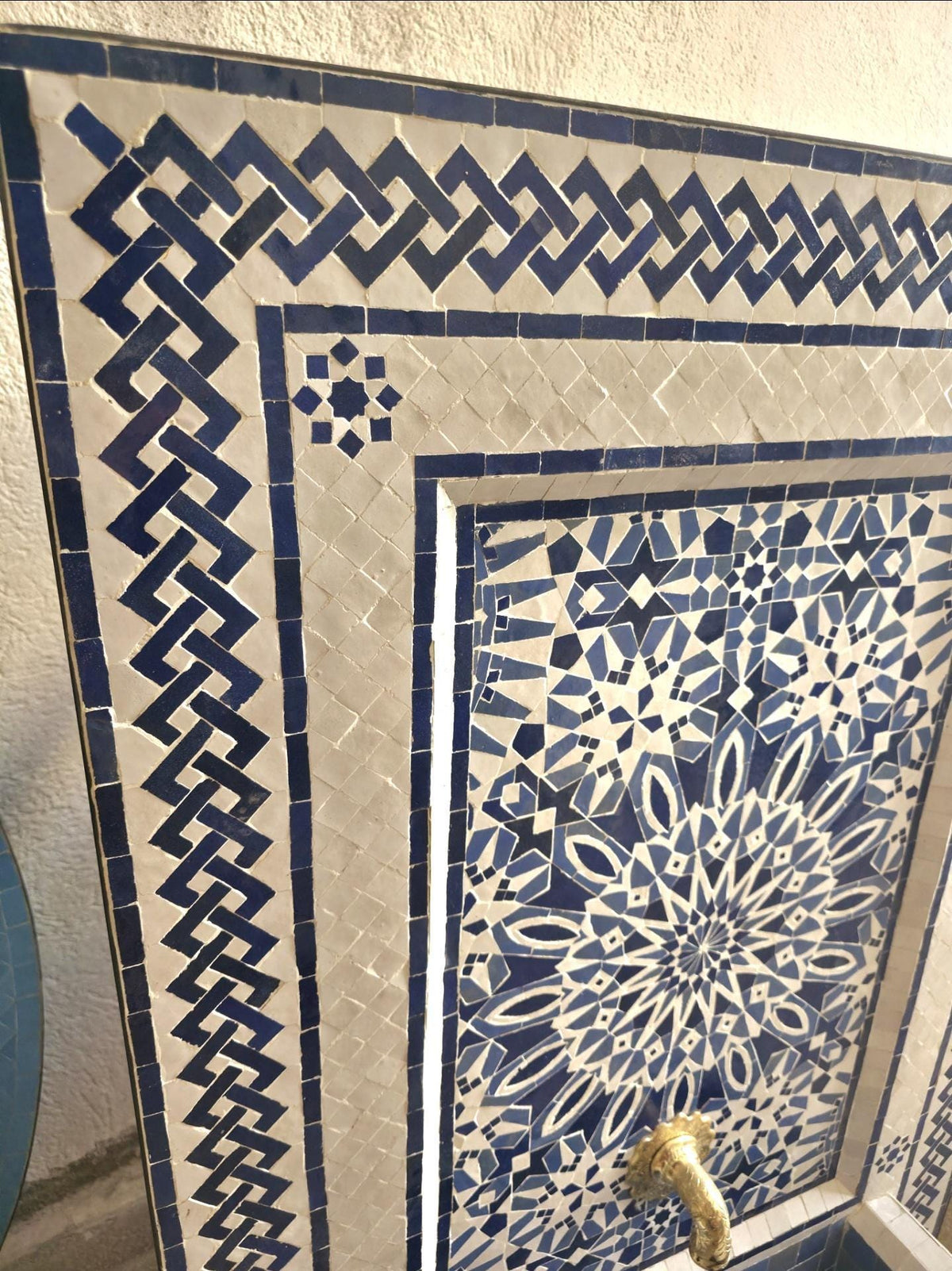 The handmade zellige fountain in action, water streaming from the brass spout into the blue tiled octagonal basin, a calming Moroccan courtyard water feature.