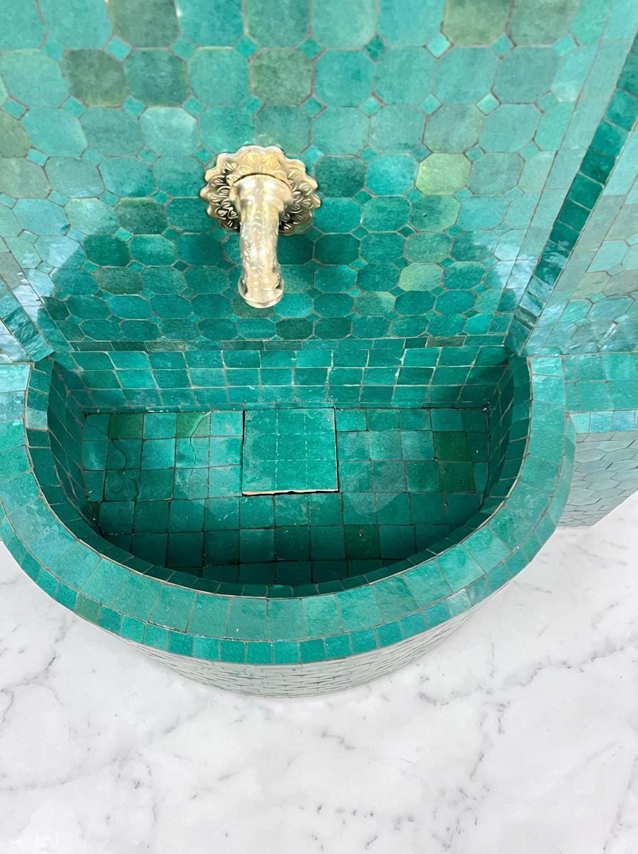 a green mosaic tile wall with a gold-colored faucet on top.
